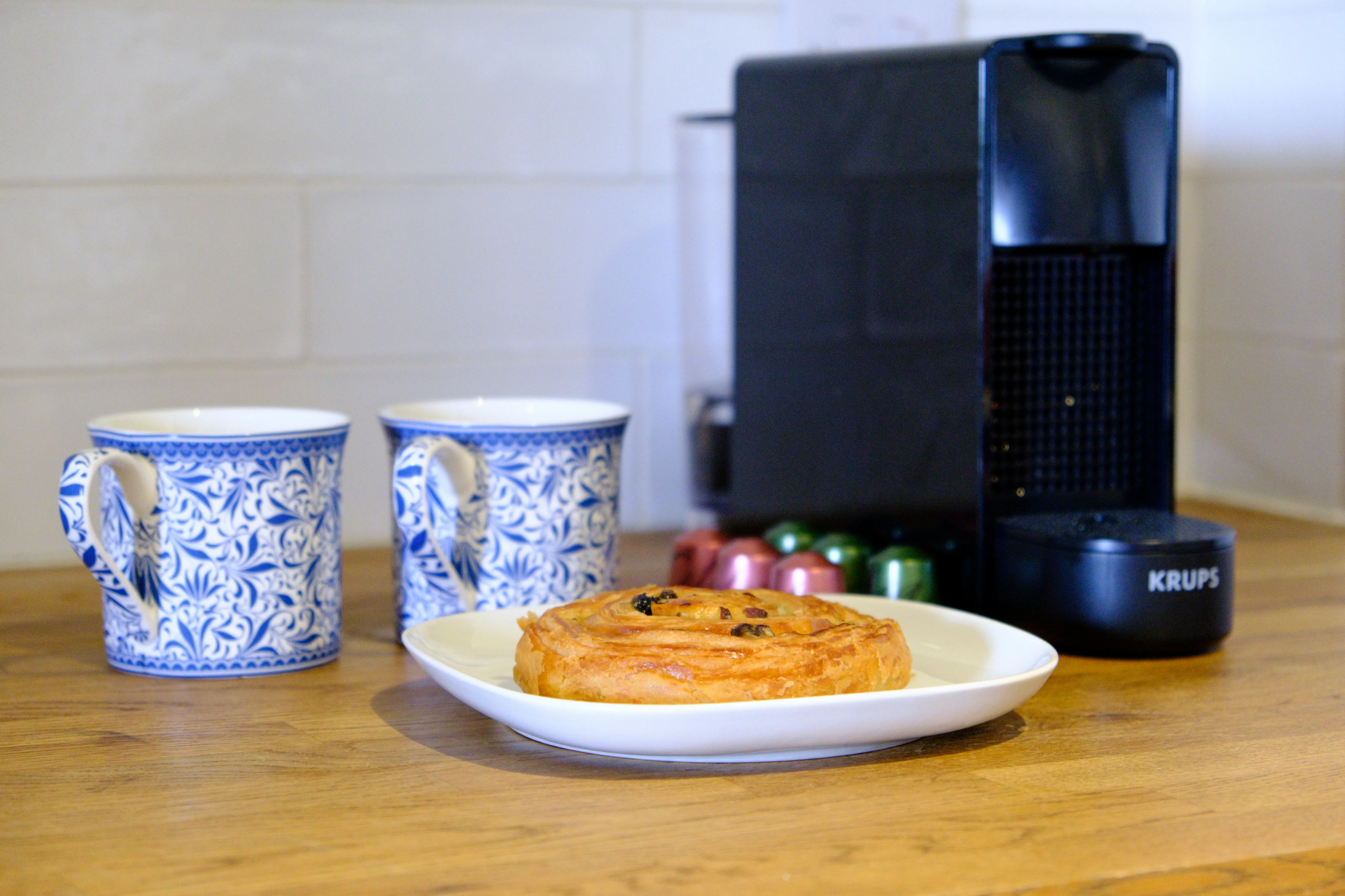 A pain aux raisin on a plate with two coffees.