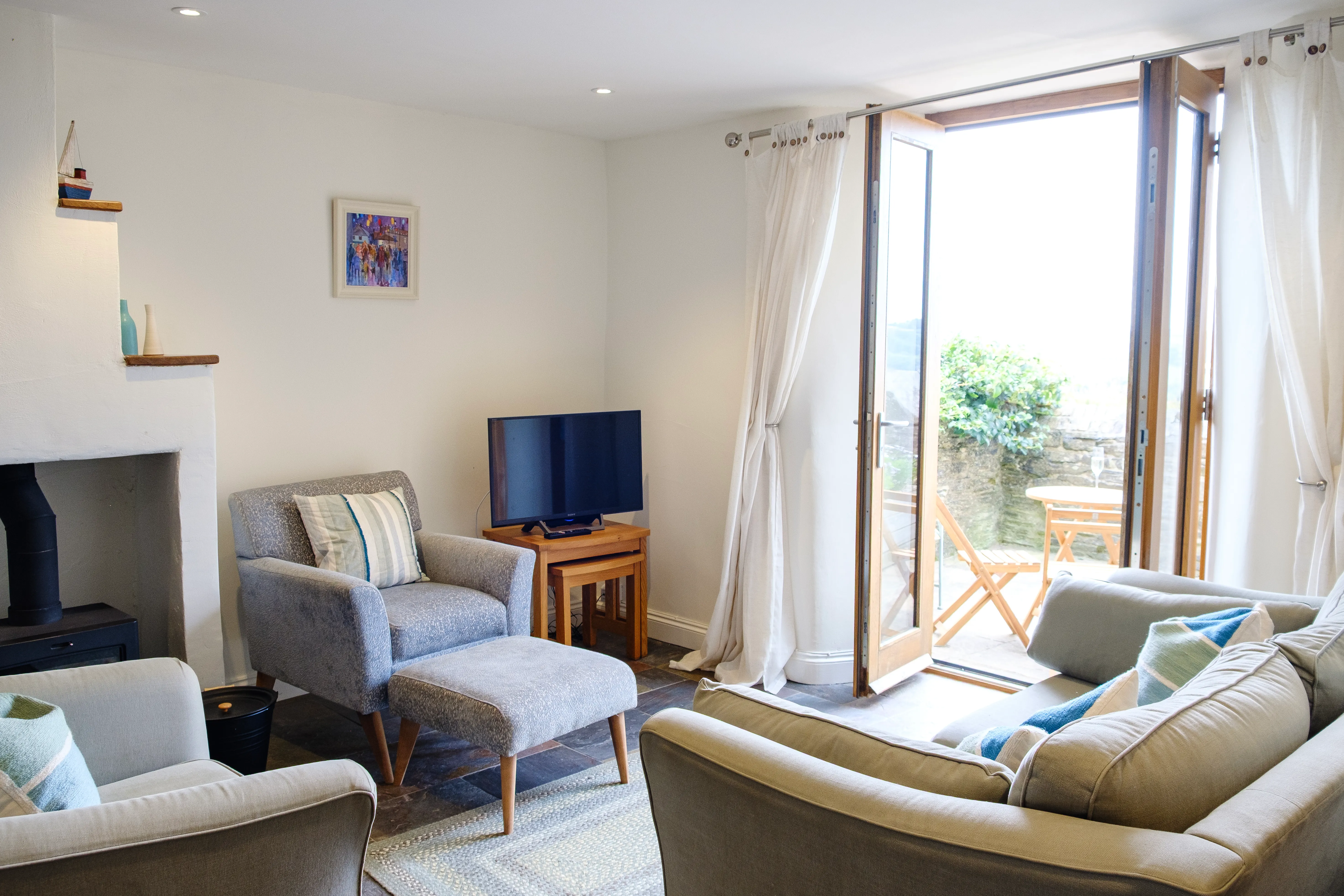 Cosy living room with light coloured walls, a quirky fireplace, and open doors onto the courtyard
